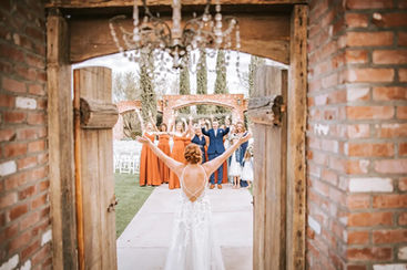 Bride throws her arms wide as she bursts through Windmill Winery's iconic barn doors, the wedding party erupting in cheers along the brick aqueduct path.