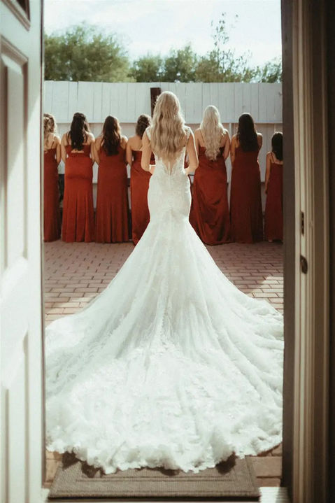 Bride approaches her bridesmaids in burnt orange satin from behind for the first look at Windmill Winery, lace cathedral train spread across the brick path.