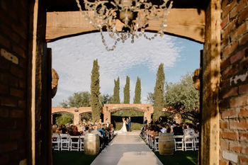 Through the timber breezeway and crystal chandelier of Windmill Winery, sunset light spills over the brick aqueduct ceremony arches and seated guests.
