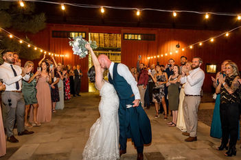 A groom dips his bride for a kiss as guests cheer beneath bistro string lights outside the iconic red barn at Windmill Winery, bouquet raised in triumph.