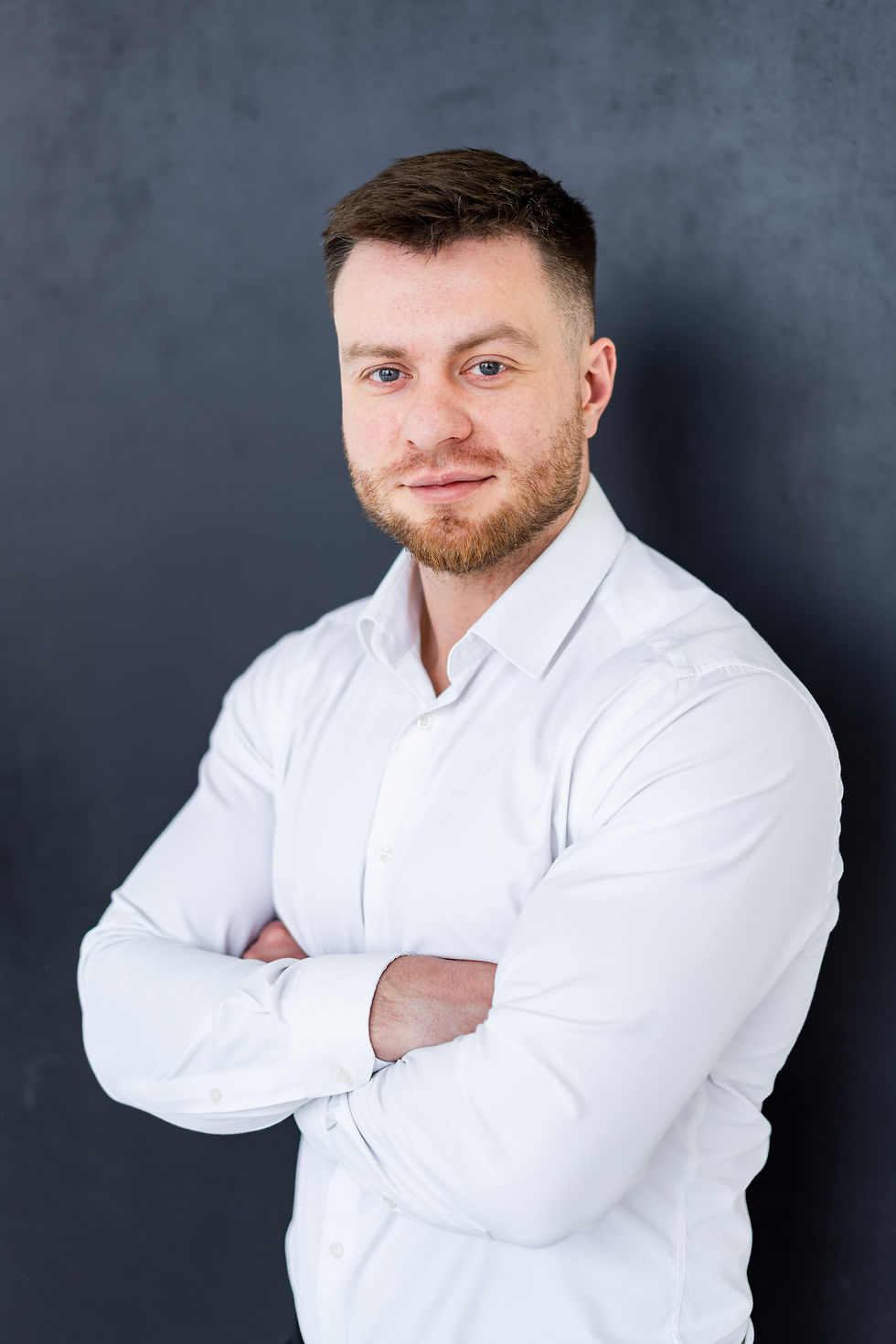 confident-man-poses-indoors-confident-man-with-groomed-beard-stands-with-arms-crossed-whit