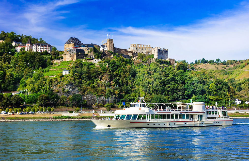 A river cruise ship sailing on the Rhine River with Marksburg Castle perched on a hill above the riverbank in Germany under a clear blue sky.