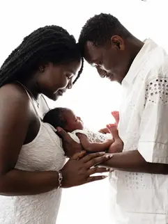 Close-up of baby snuggled between parents’ hands, surrounded by warmth
