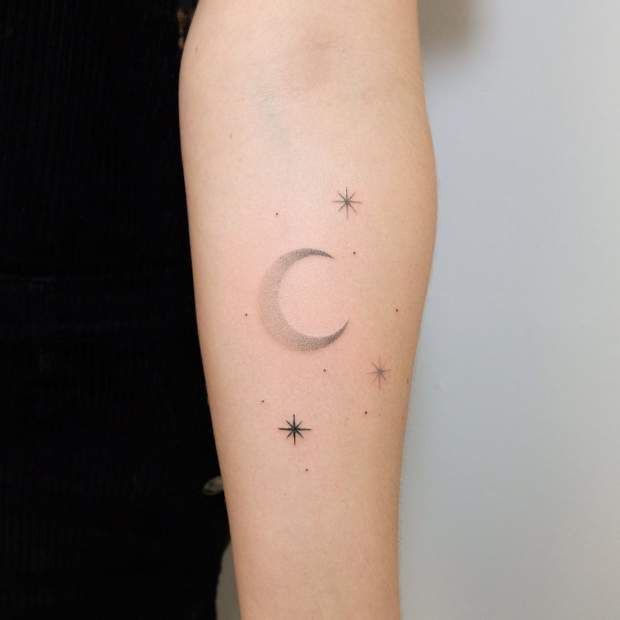 simple small classy moon forearm tattoo lightly shaded with small stars