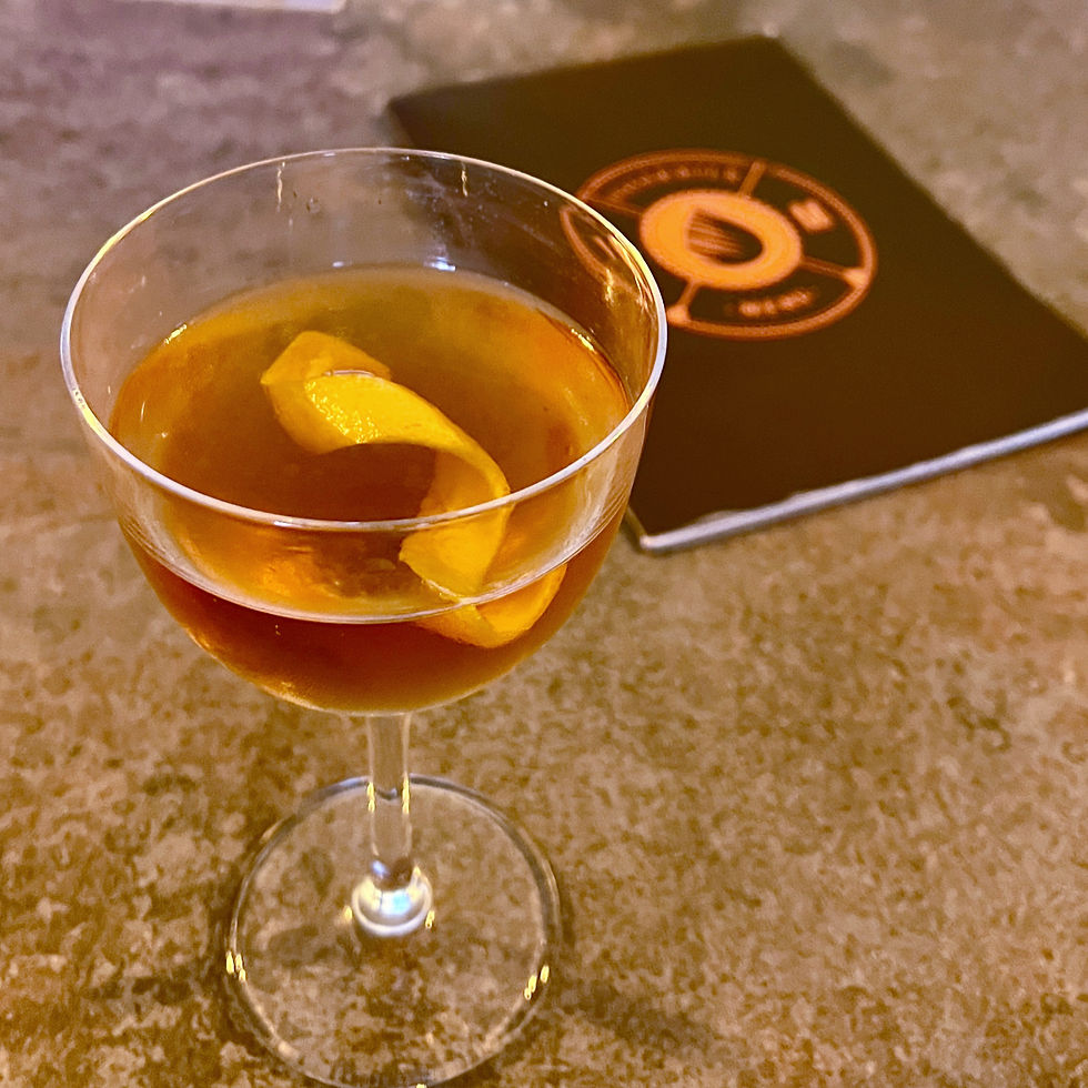 A coupe glass with a golden-brown cocktail and orange twist sit on the bar at Tiger Milk, Plymouth