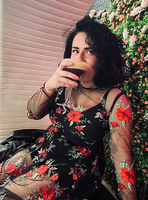 Grace sits in a floral dress, sipping an espresso martini
