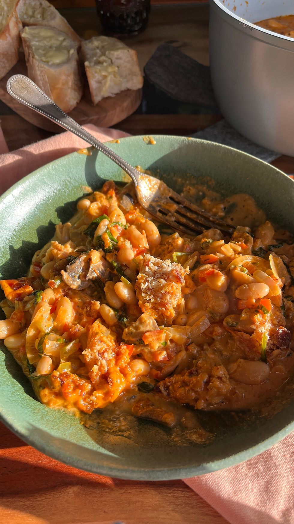 A bowl of warm, creamy, tuscan bean stew is served with some buttered baguette. 