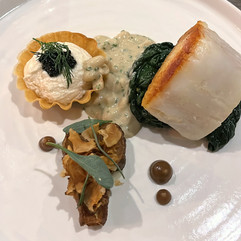 A white plate with pan-fried cod, sauteed greens, taramasalata tartlet