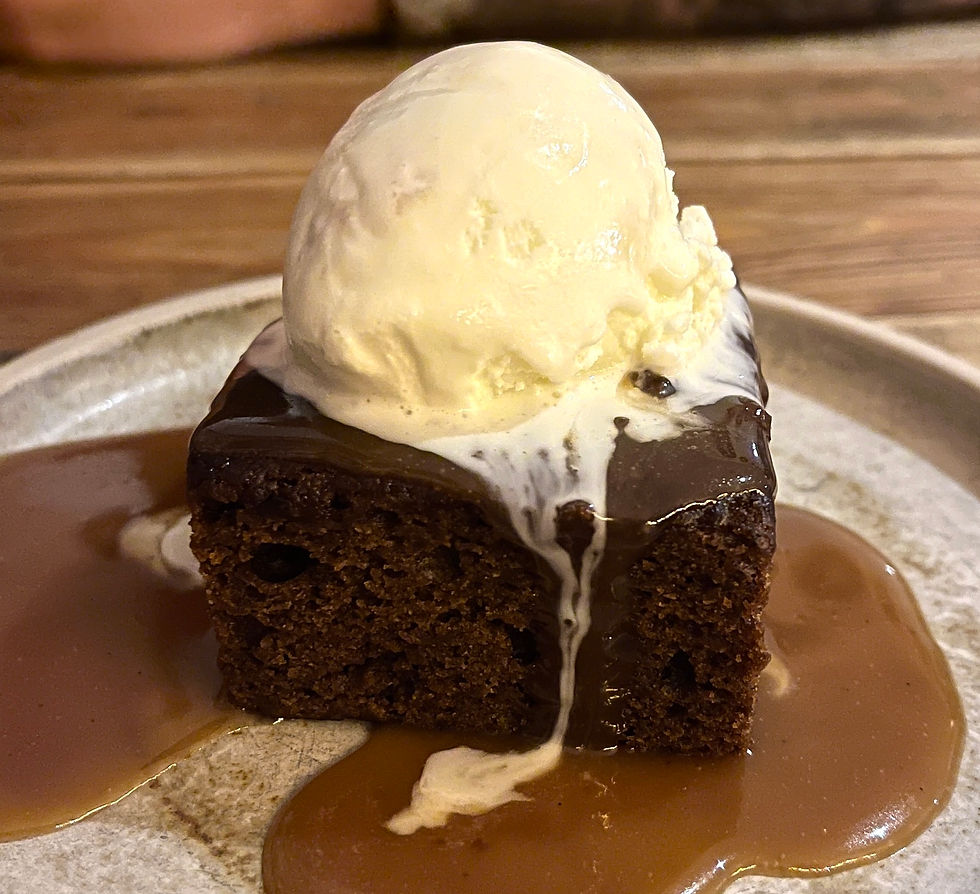 A plate of sticky toffee pudding. The dark spiced sponge is coated with a thick, salted caramel sauce and topped with a large scoop of honeycomb ice cream