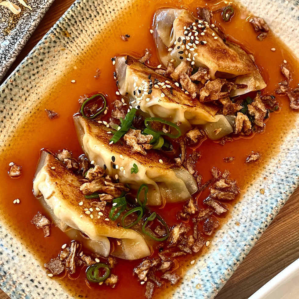 Chicken gyoza dumplings rest in a soy sauce on a tray at Kuku in Plymouth