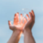 Hands holding string lights against a blue sky.
