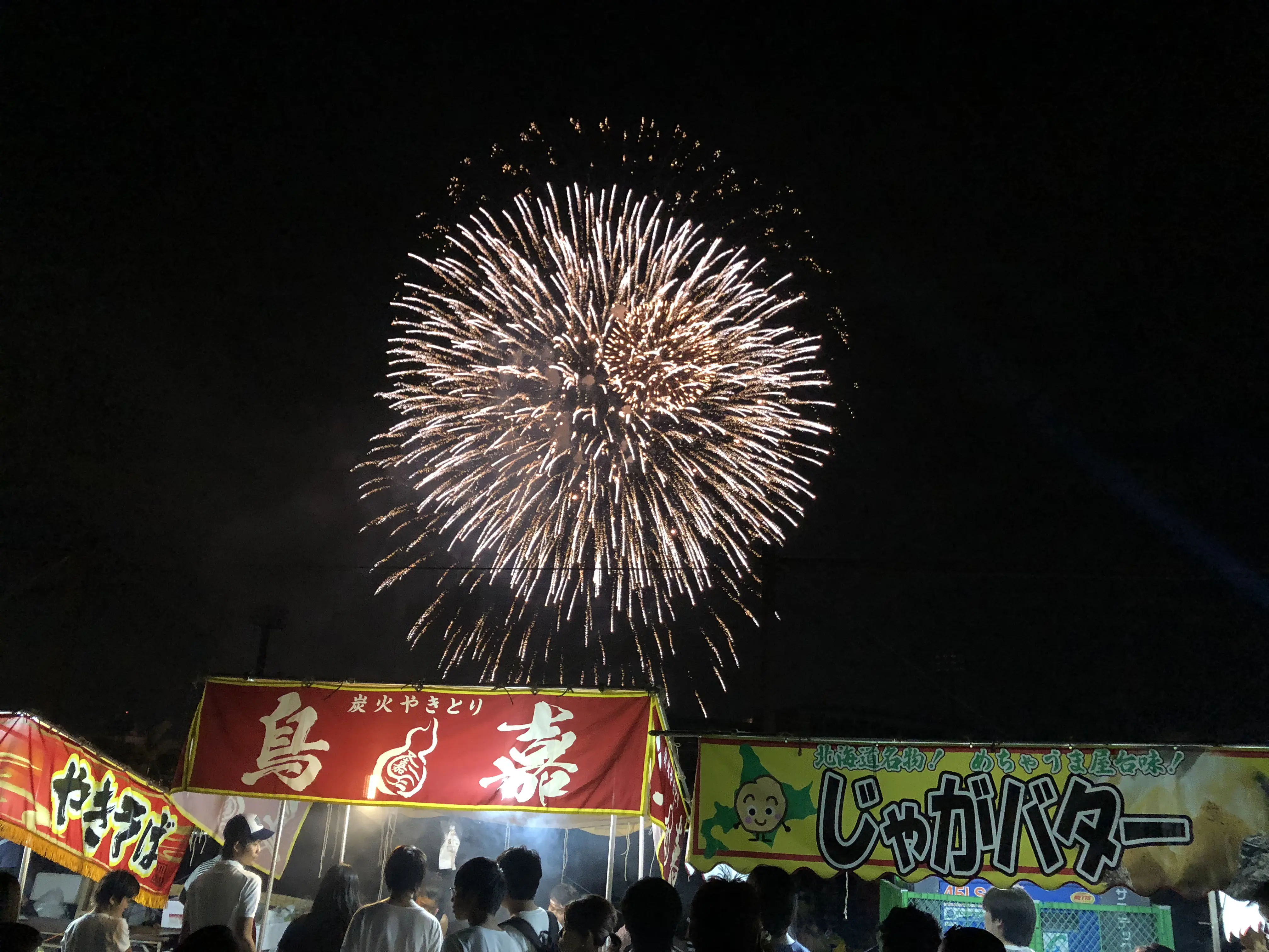 Summer fireworks festival in Japan with hanabi lighting up the night sky above traditional food stalls.