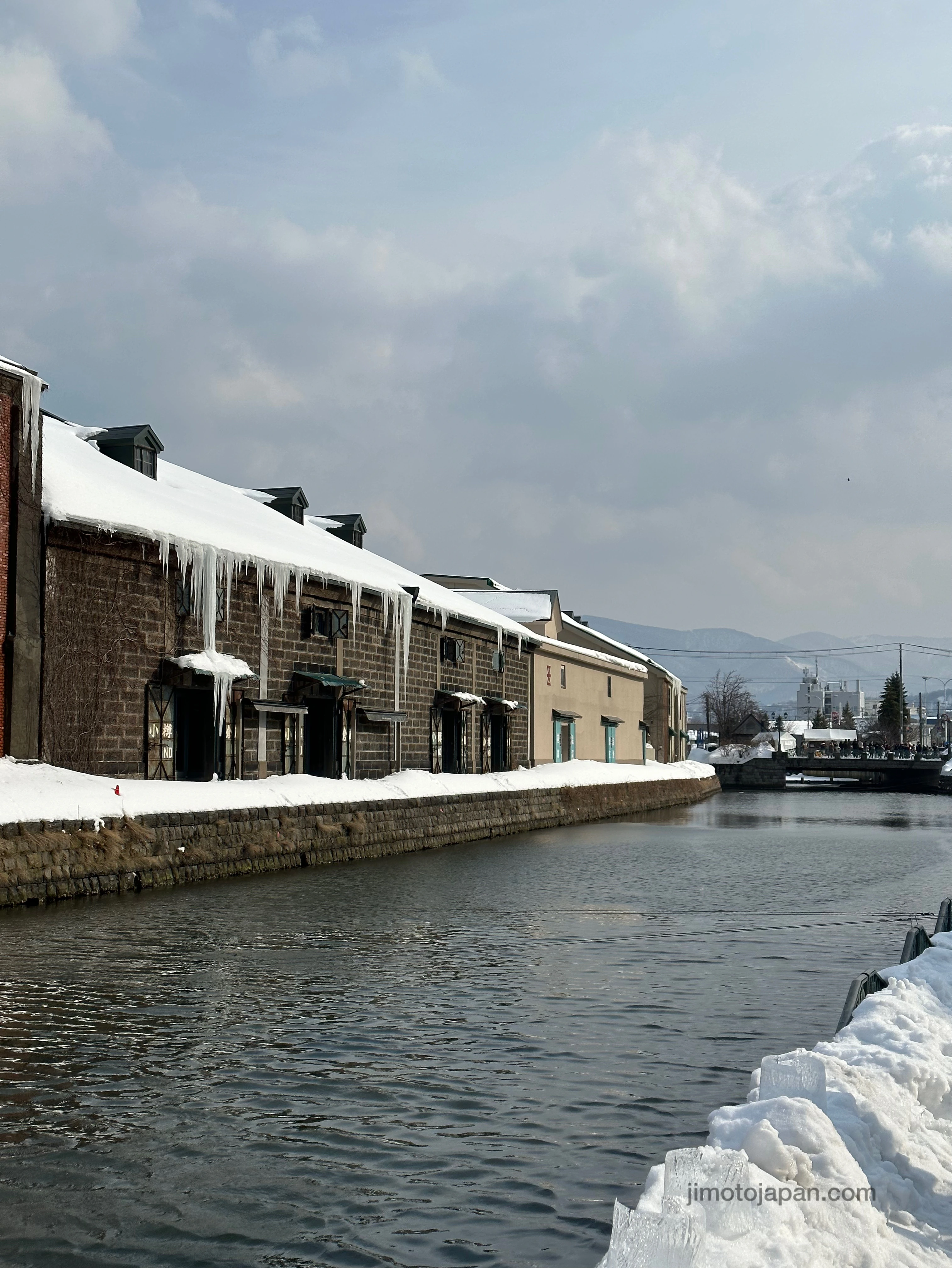 Snow-covered warehouses along Otaru Canal during winter daylight.