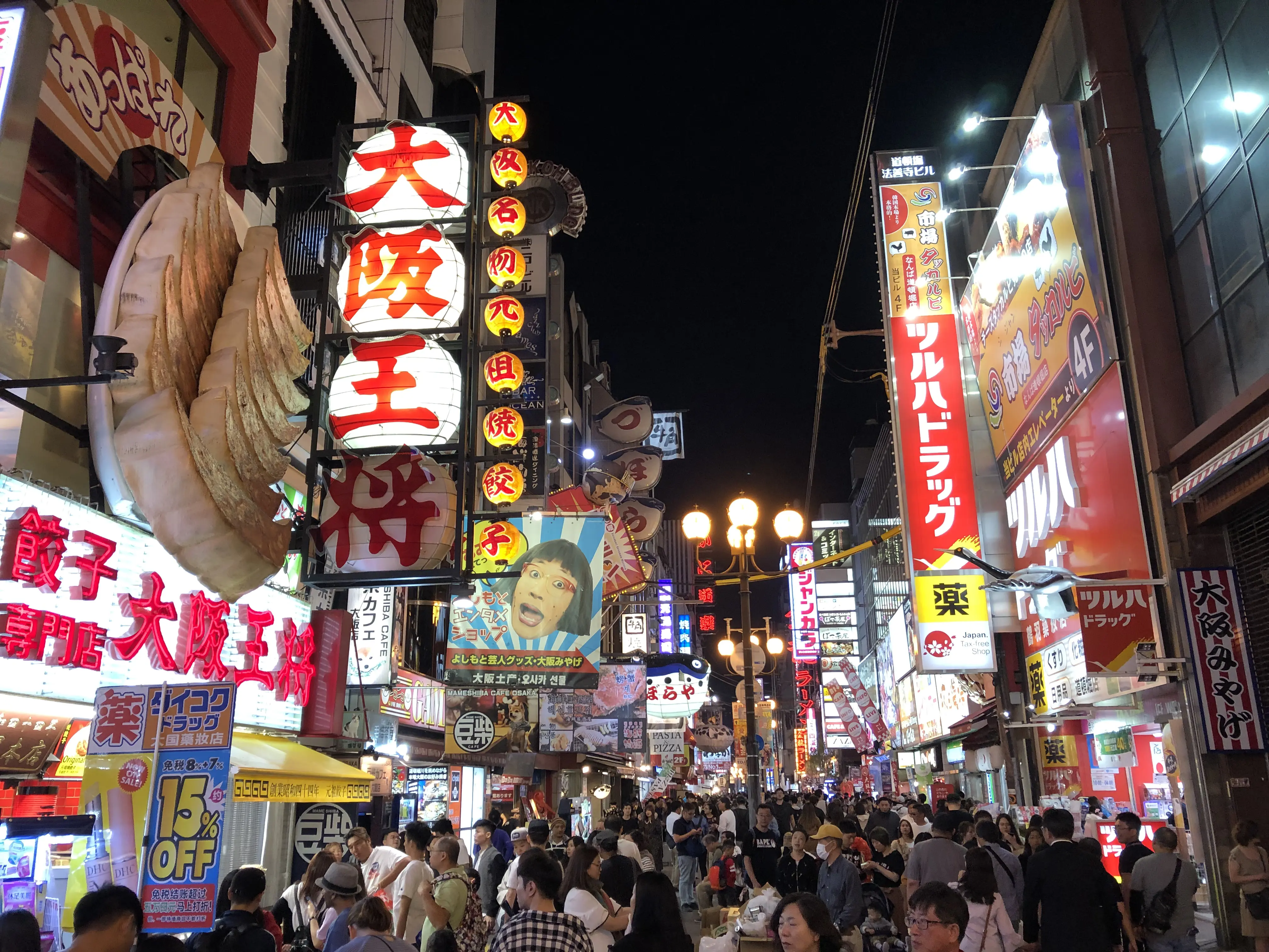 Busy nightlife street in Japan with neon signs and crowds, showing a popular tourist area where cash and cards are both commonly used