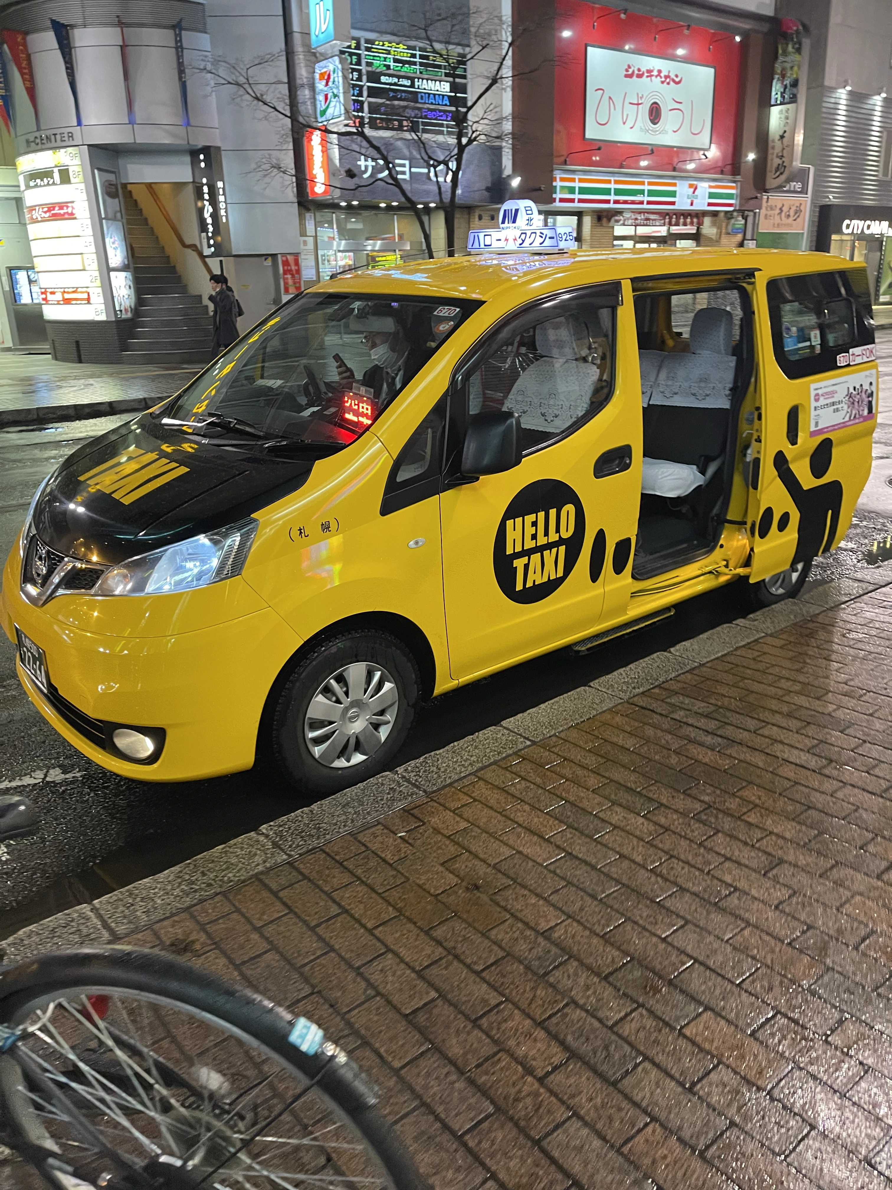 Yellow taxi in Japan at night in a busy city area, showing modern taxi services where credit cards are commonly accepted