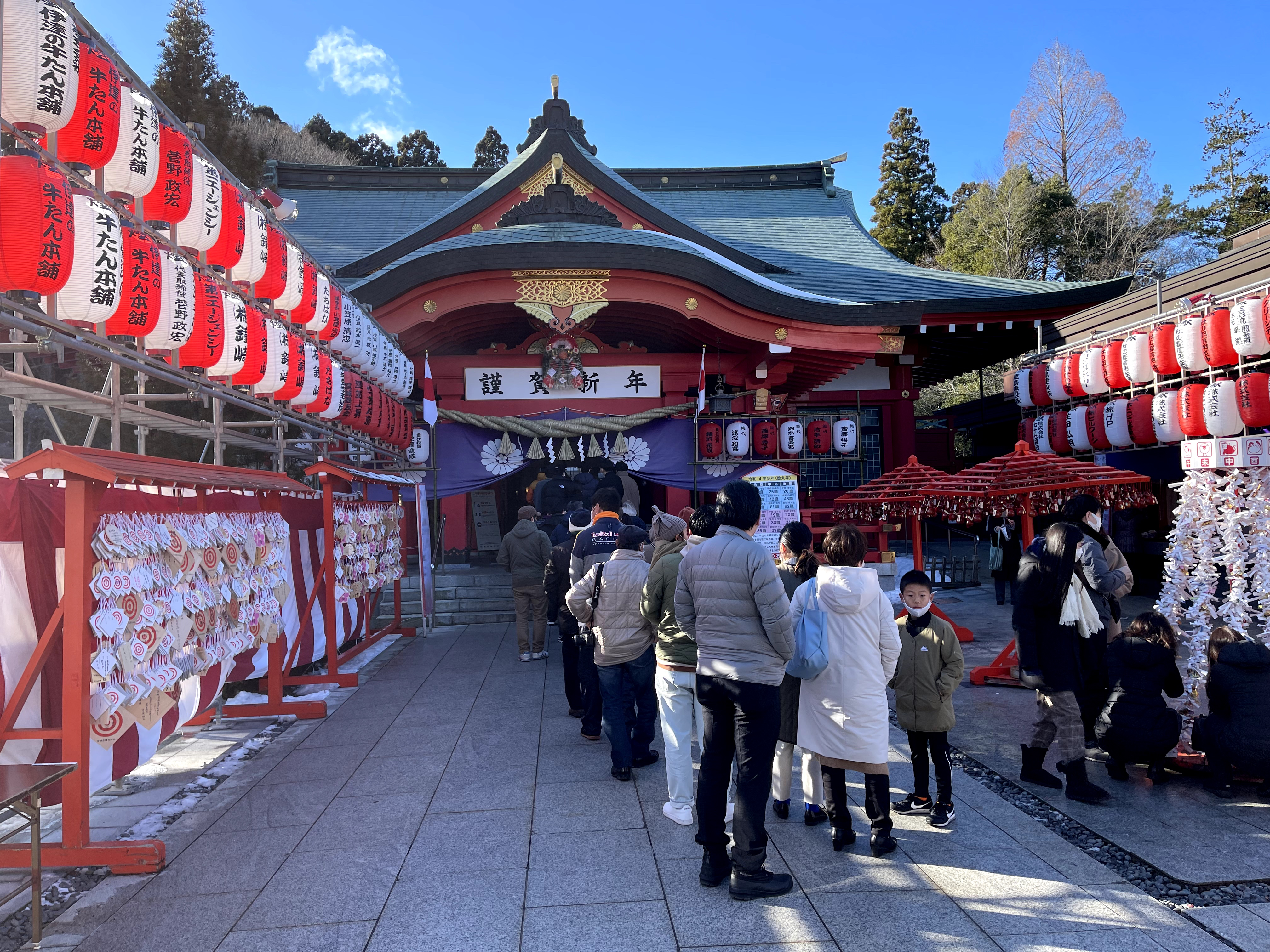 People visiting a Japanese shrine with lanterns and donation areas, showing traditional attractions where cash and coins are commonly used