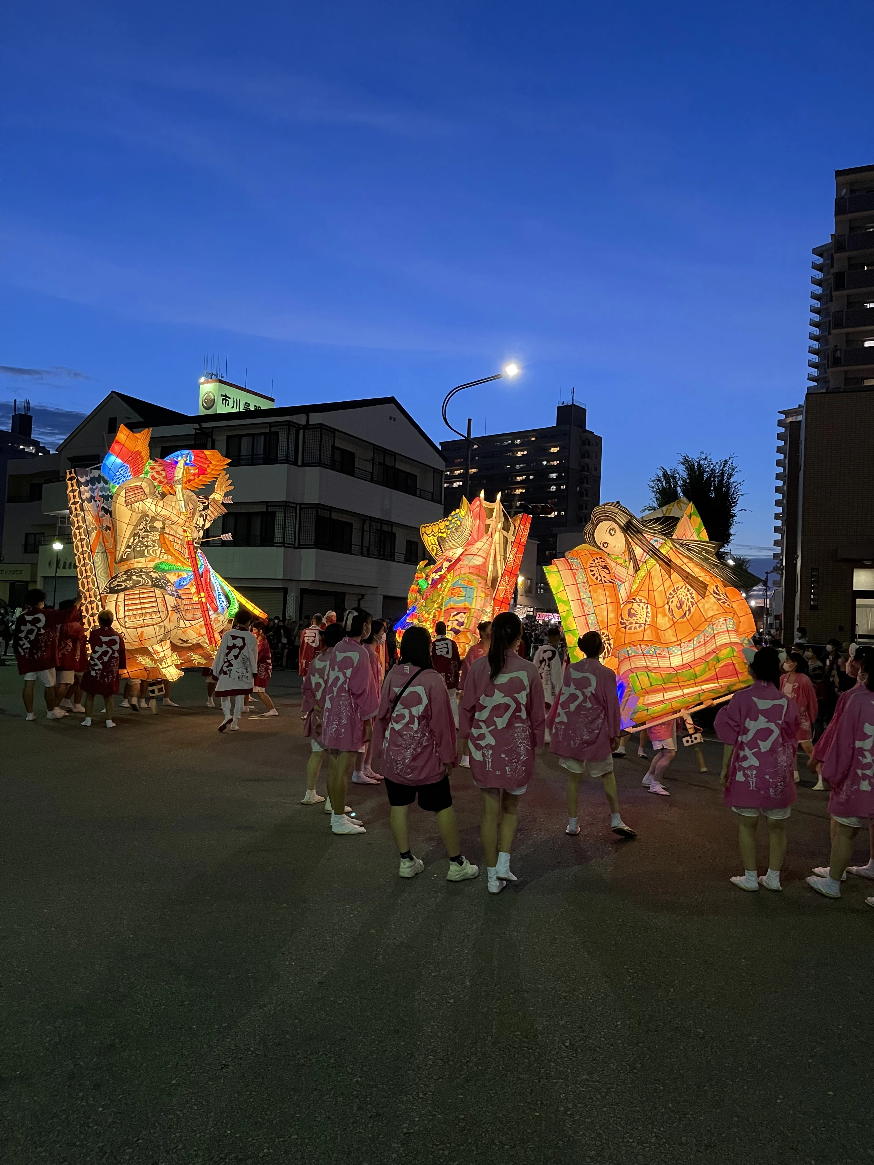 Traditional summer festival in Japan with illuminated floats and locals wearing happi coats at night.