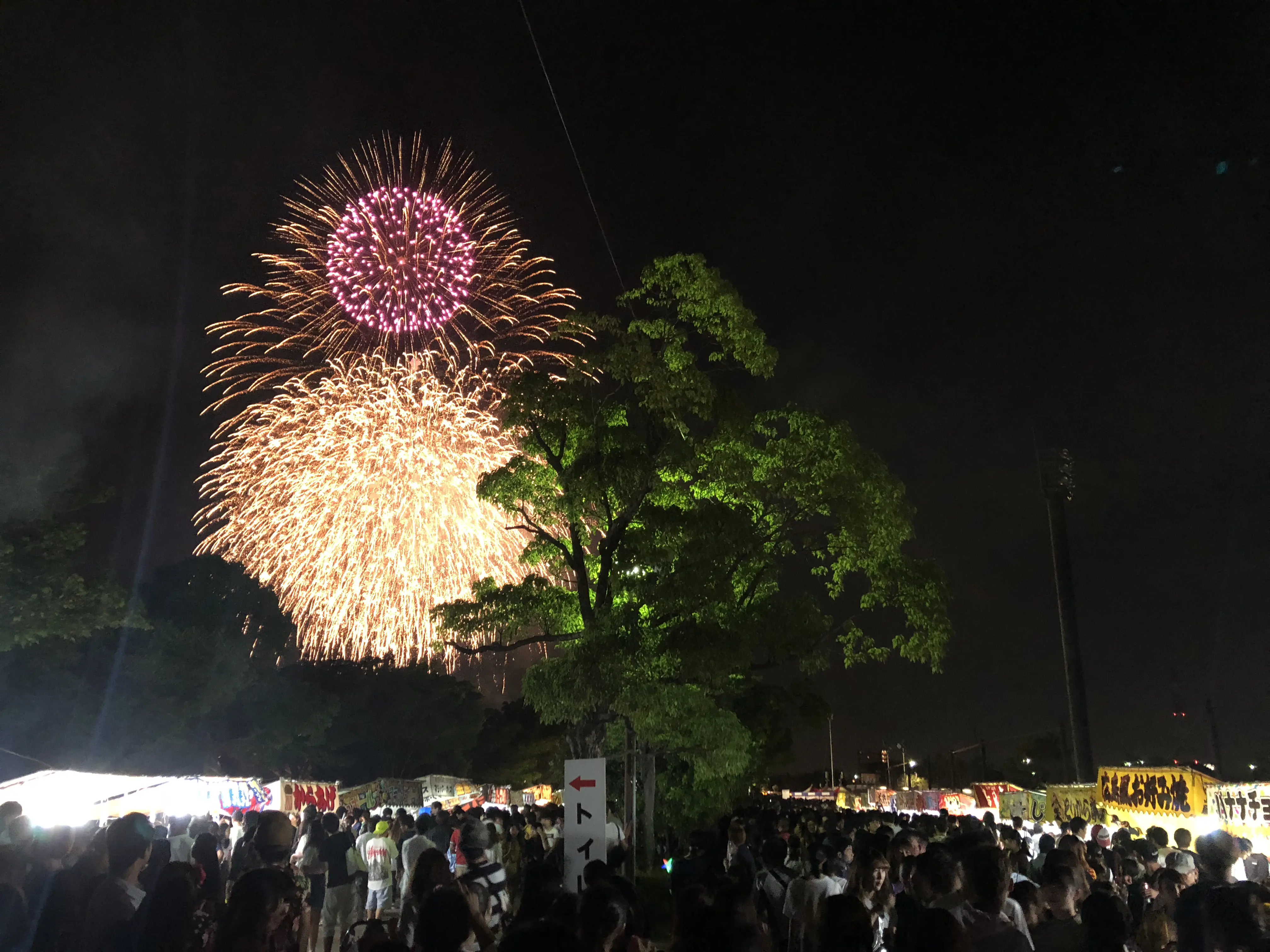 Summer fireworks festival in Japan with hanabi lighting up the night sky above traditional food stalls.
