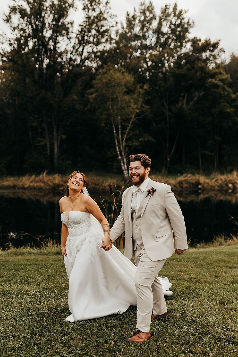 Bride and groom smiling under the trees by the lake at a waterfront Michigan wedding venue.