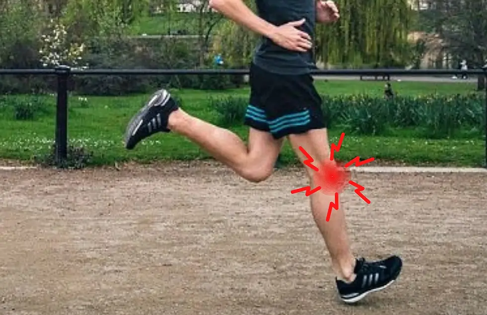 Runner in black shorts and sneakers sprinting on a park path, with a red pain marker on the knee.