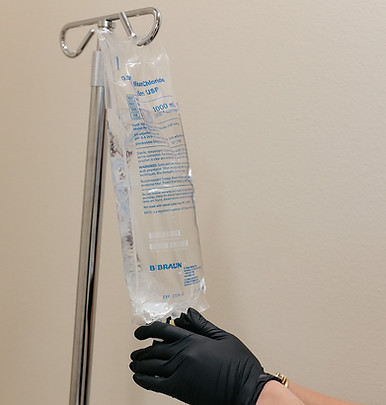 Gloved hands adjusting an IV vitamin therapy bag on a stand.