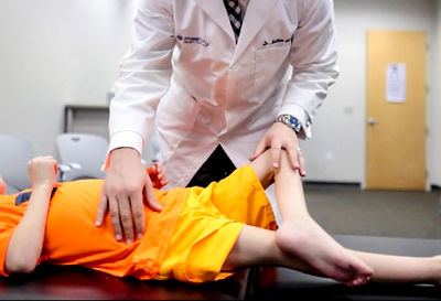 Doctor Kornfeld in a white coat examines a child in orange clothing on a table in a bright room. Calm and focused atmosphere.