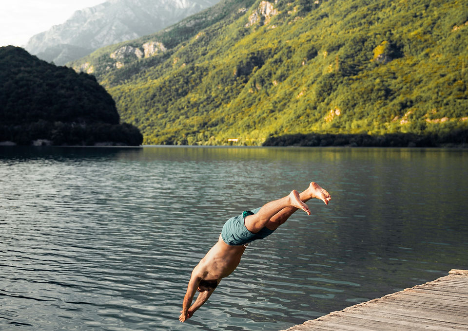 Man diving into a lake near lush green mountains.