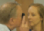 Doctor examines woman's eye with an ophthalmoscope in a clinic. Both appear focused. Neutral-toned background.