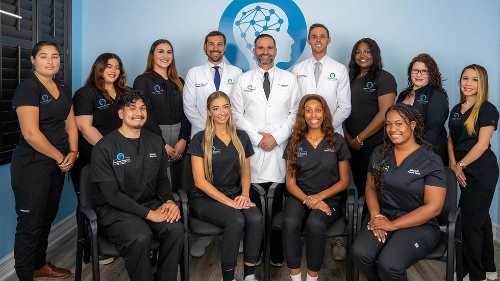 A team of functional neurology brain center of Florida in uniforms and lab coats pose smiling in a blue room.