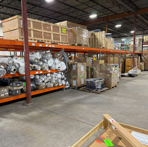 Warehouse interior with shelves of boxes and rolls of fabric. Concrete floor, high ceiling with lights. Labels on boxes, organized setting of Design Logistics Group Warehouse