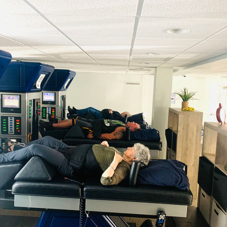 People lie on therapy beds in a clinic with DRX9000. Neutral mood, bright setting, and visible screens and controls on each device.