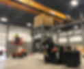 Overhead crane lifts a pallet while workers operate a forklift and scissor lift