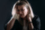 Woman with blonde hair holds head in hands, visibly distressed. Bandaged wrist, dark background, emotional tension.
