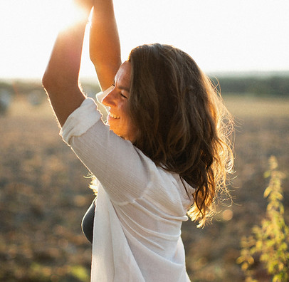 Woman smiling with arms raised in golden sunset light.