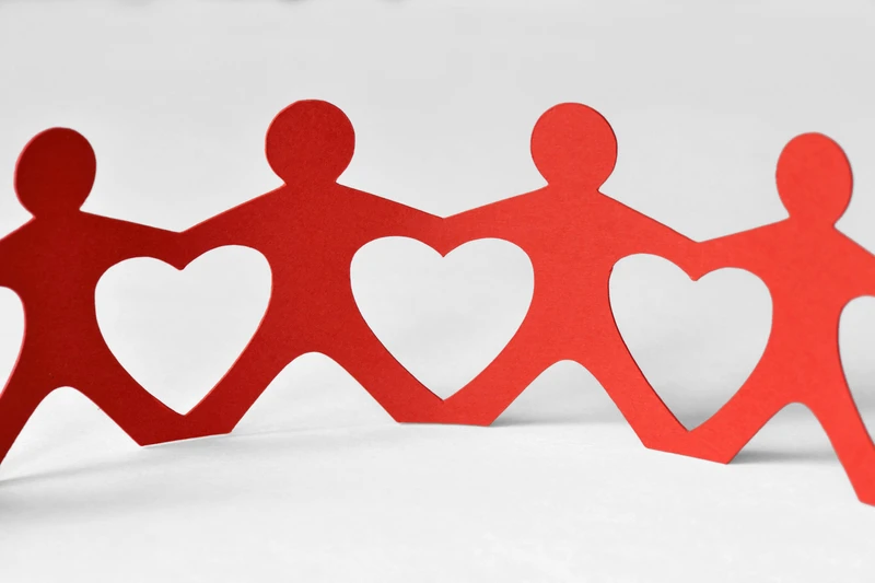 Paper cutout of people holding hands creating heart shapes between them