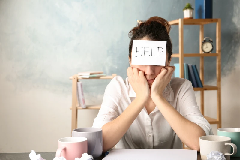 Woman in burnout at desk with help sign on her forehead
