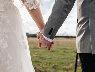 a couple holding hands wearing their wedding attire in front of the farmlands.
