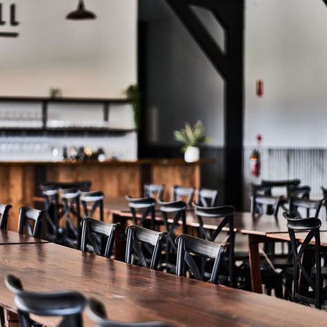 Empty hall with wooden tables, black chairs, and plants in pots. Shelves with glasses behind the bar, sign reads "LEONARDS HILL ESTATE."