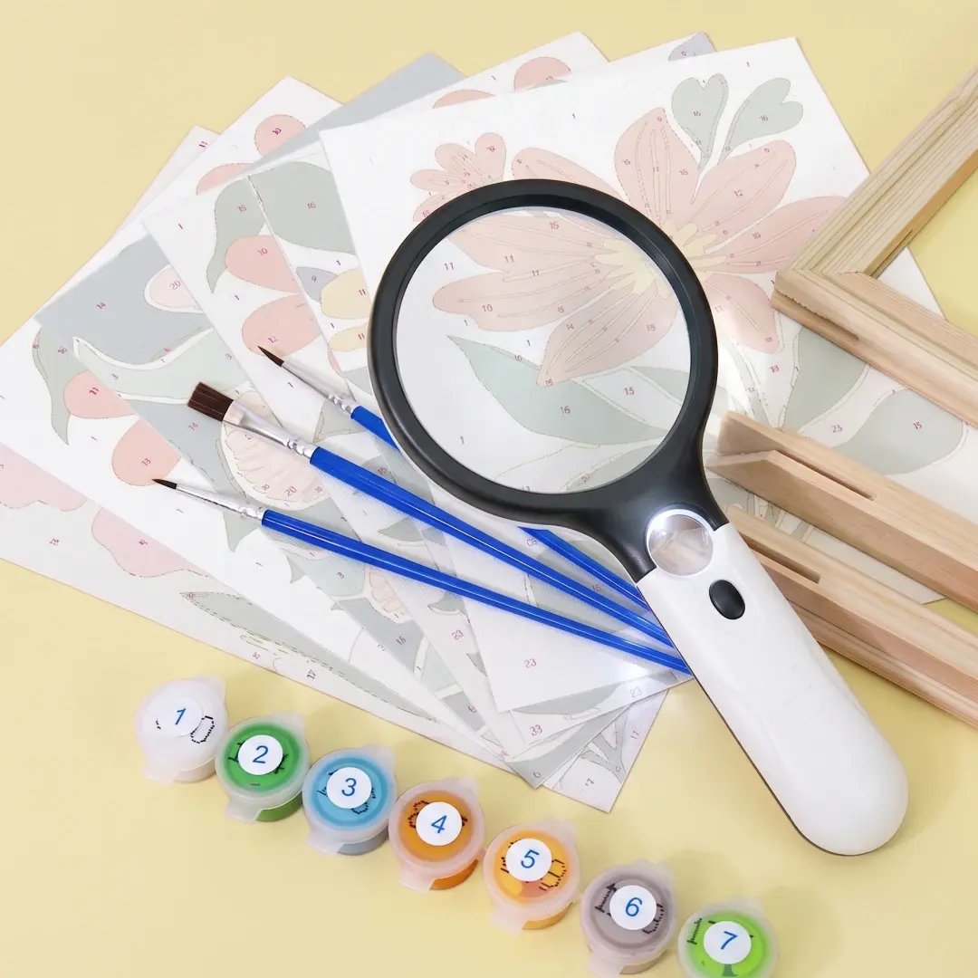 LED handheld magnifying glass resting on a floral paint by numbers canvas next to paint pots and brushes