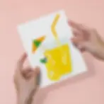 Hands holding a finished lemon juice drink canvas paint by numbers kit.