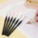 A hand using a triangular ergonomic detail brush to paint a paint by numbers canvas