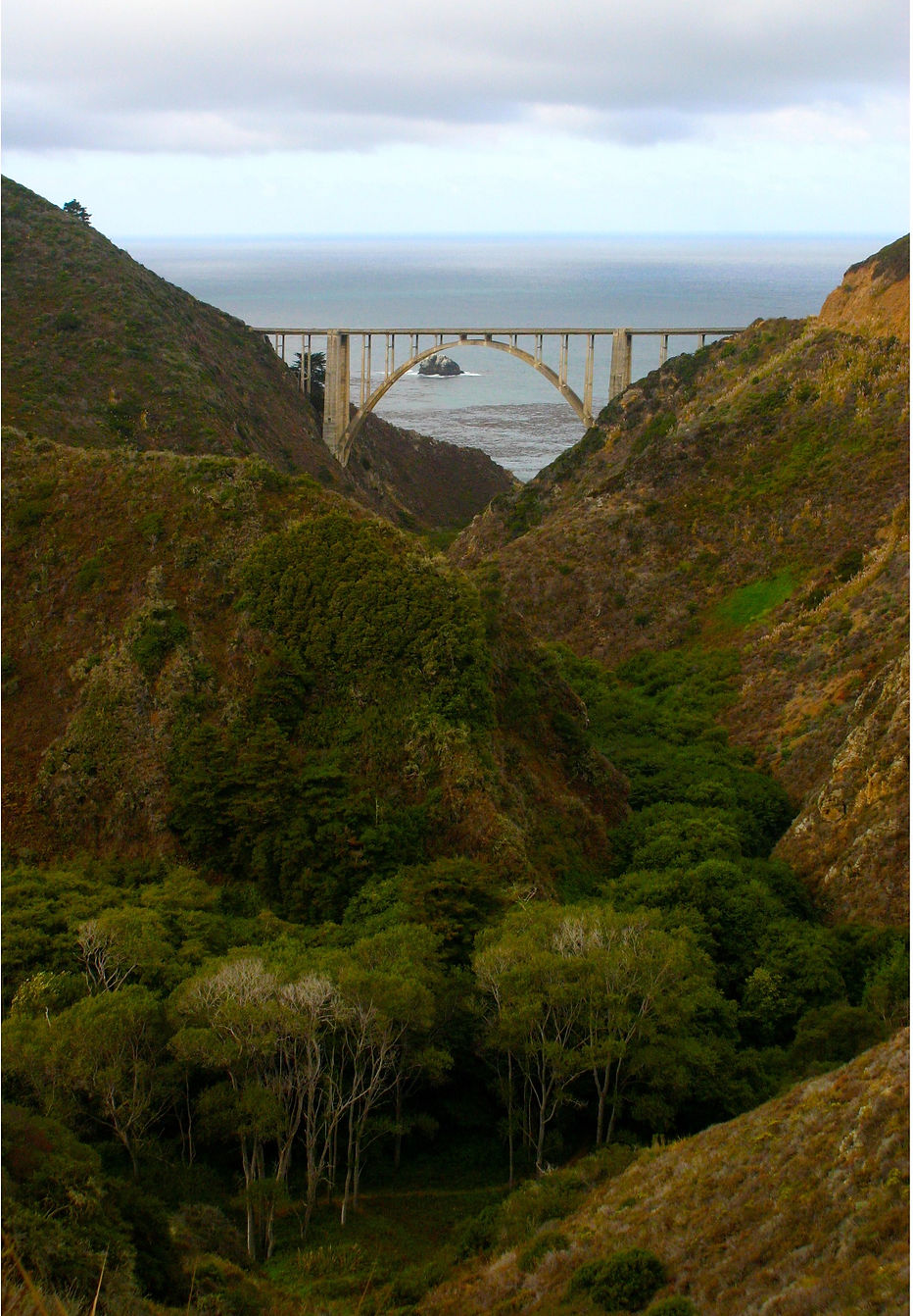 Color photograph by Peter Keresztury of the Bixby Creek Bridge through the trees. SIgned, titled, matted and framed
