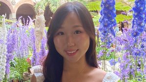 Isabella Park smiles while standing in front of tall purple flowers