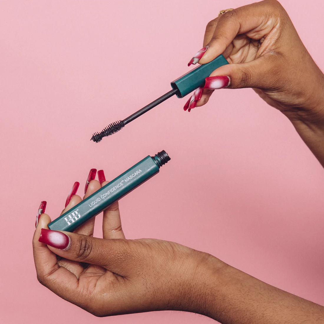 Two hands holding the wand and tube of mascara
