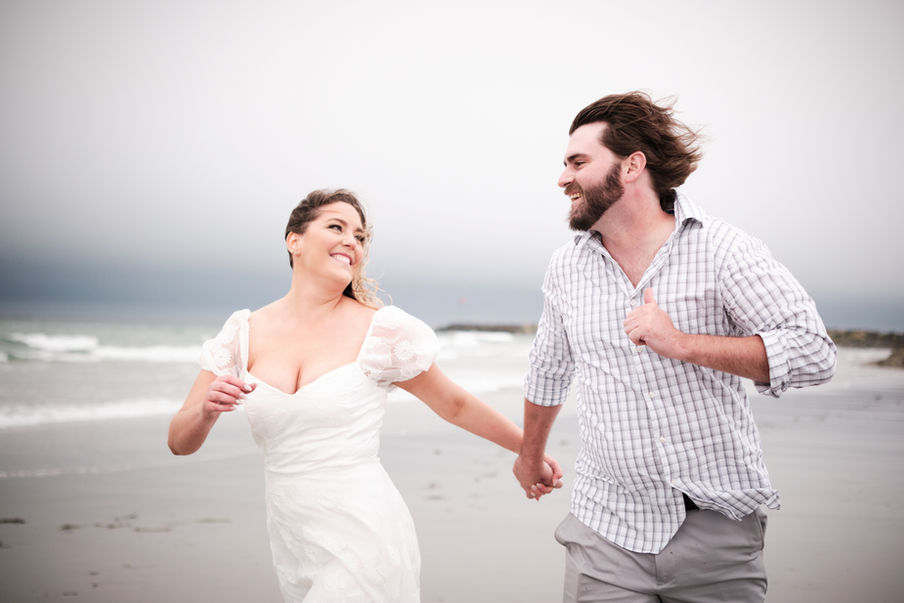Golden hour engagement photography of a couple running on the beach at Hampton Beach State Park in Hampton Beach, New Hampshire, captured by Storm Raven Photography.