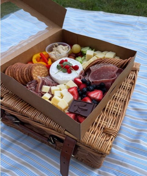 Wicker basket with a box on top of it filled with prepared Charcuterie and Fresh Produce