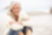 A healthy middle-aged woman sitting with her crossed arms resting on her knees on the beach. Dr. Kara A. Boas's office in Morganville Square is located a short drive from Jersey Shore beaches.