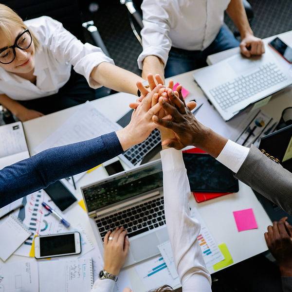 Overhead view of four hands joined in a circle over a desk, symbolizing leadership, growth, and communication.