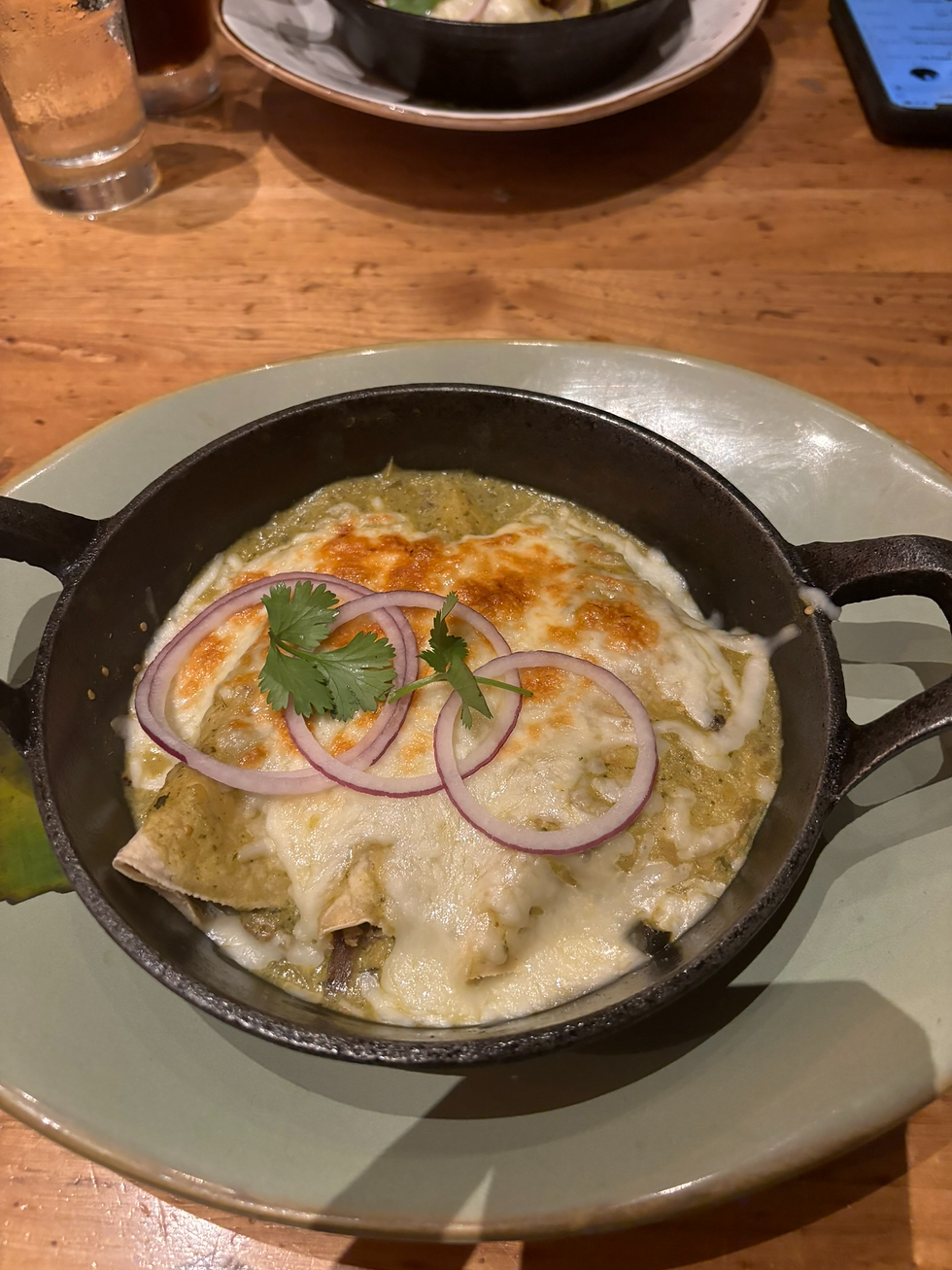 Creamy Chicken Enchiladas Suizas, featuring enchiladas smothered in a tomatillo cream sauce and topped with Queso Chihuahua, fresh cilantro, and rings of red onion in a black cast iron skillet.