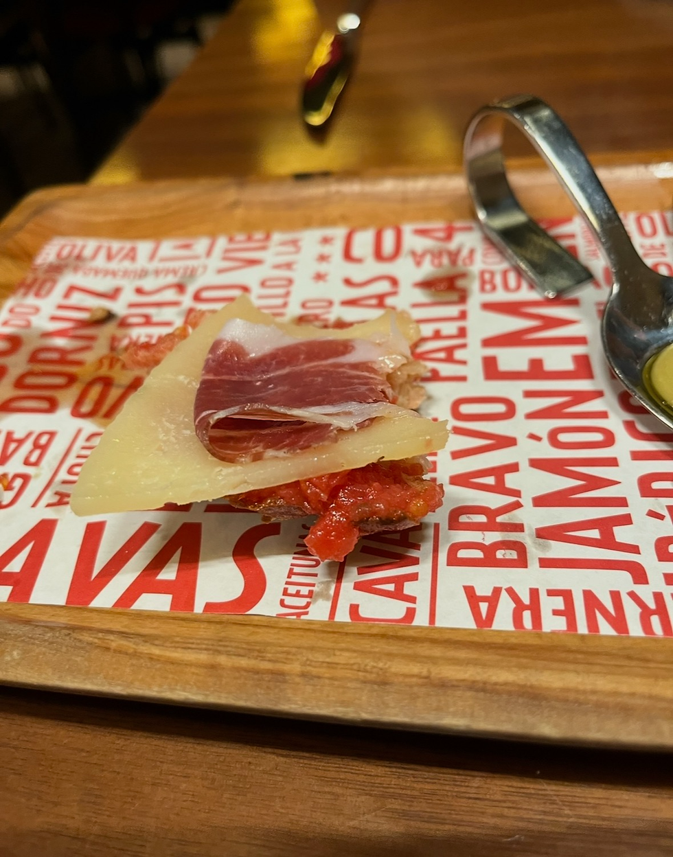 Pan con Tomate con Jamón y Queso, which has a peice of toasted bread, crushed tomato, a thin slice of cured ham, and a shaving of cheese.